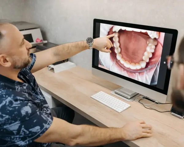 Dentysta omawia z pacjentem czyszczenie kieszonek dziąsłowych, wskazując na zbliżenie jamy ustnej na monitorze.
