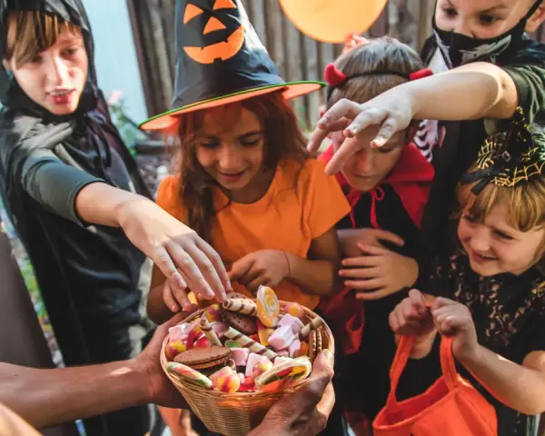 Barn i Halloween-kostymer sträcker sig efter godis ur en korg. Det är en klassisk "bus eller godis"-kväll!