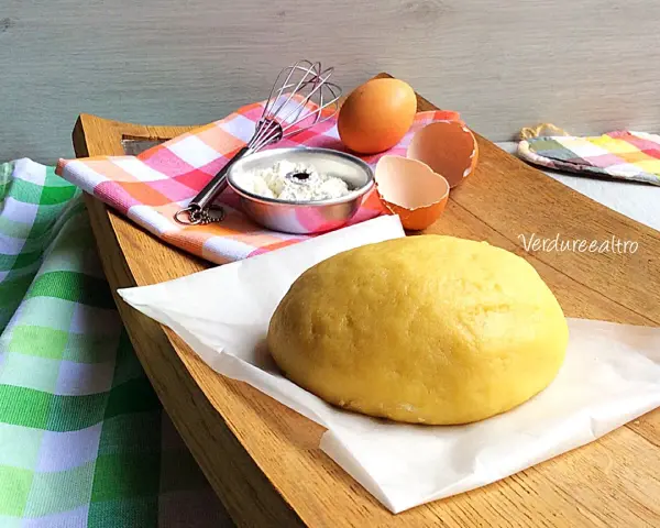 Impasto giallo pronto per essere lavorato, con uova e farina a lato. La pasta frolla senza burro è perfetta per dolci leggeri.