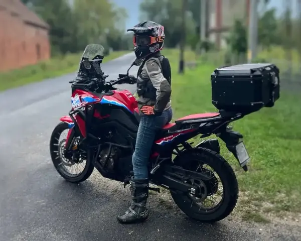 Motocyklistka w kasku i z kufrem na bagażniku gotowa na wyprawę po Kaszubach.
