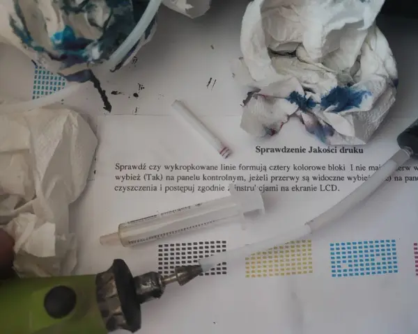 Narzędzia do automatycznego czyszczenia drukarki Brother: strzykawka, papierowe ręczniki z atramentem i instrukcja "Sprawdzenie Jakości druku".