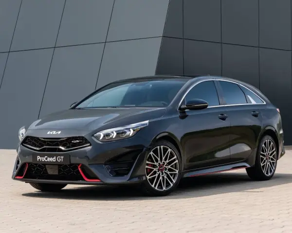 Stylowy, ciemnoszary Kia Proceed GT z czerwonymi akcentami i sportowymi felgami, zaparkowany przed nowoczesnym budynkiem.