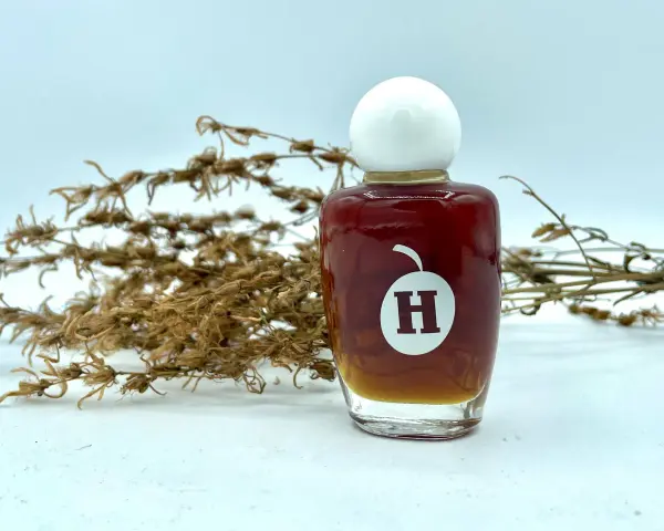 Frasco de aceite de hiperico con tapa blanca, junto a ramas secas.