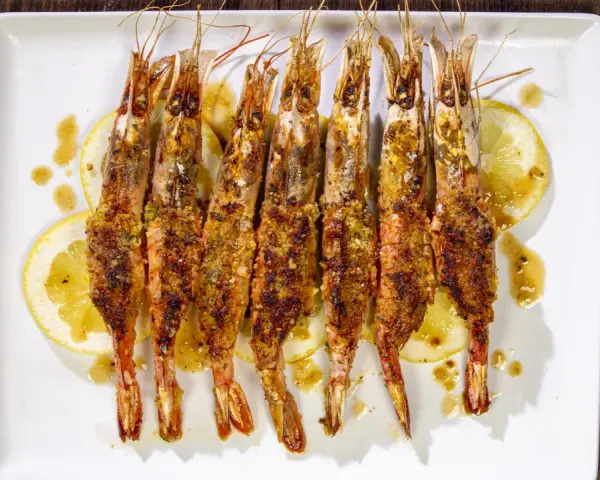 Gamberoni al forno dorati e croccanti, serviti su fette di limone e conditi con un sugo saporito.