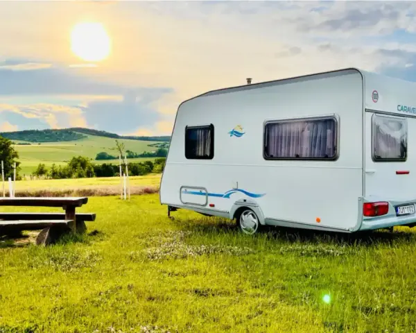 Przyczepa Caravelair zaparkowana na łące o zachodzie słońca. W tle malownicze wzgórza i pola.