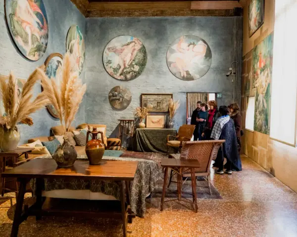 Interno del museo Palazzo Fortuny con opere d'arte alle pareti, arredi d'epoca e visitatori.