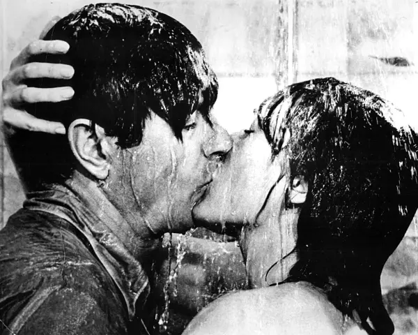 Una pareja se besa apasionadamente bajo la ducha, un momento íntimo que captura la esencia de qué es un beso francés.