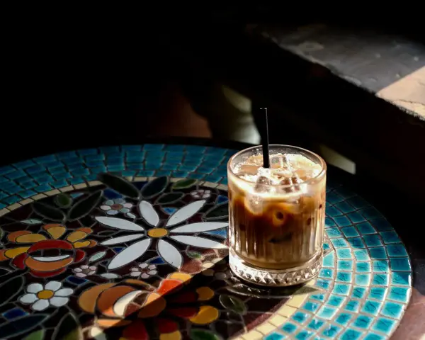 Orzeźwiający cold brew latte z lodem, podany na kolorowym, mozaikowym stoliku, w promieniach słońca.