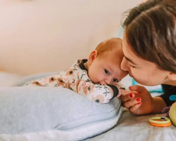 Mama pochyla się nad dzieckiem, które leży na poduszce. Szybki oddech u noworodka może być naturalny, ale czujność rodzica jest ważna.