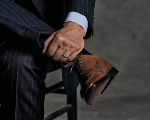 Un uomo con un abito gessato blu scuro e una camicia azzurra indossa eleganti scarpe stringate marroni.