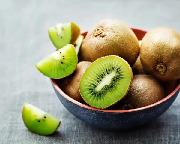 Miseczka pełna kiwi, jedno przekrojone na pół, pokazuje soczysty miąższ. Czy można jeść kiwi ze skórką? Tak, jest jadalna i pełna witamin!