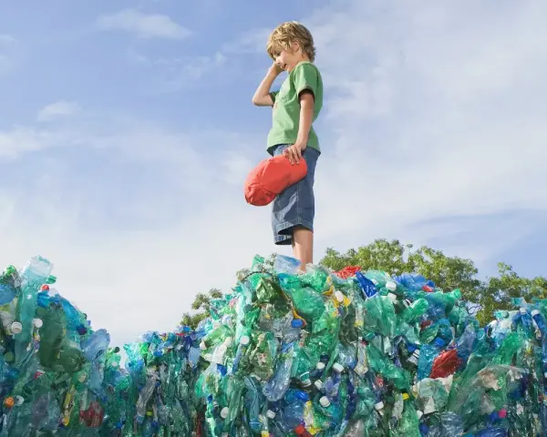 Chłopiec stoi na górze sterty plastikowych butelek, zastanawiając się, co to za pla.