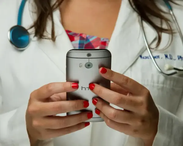 Lekarz w białym kitlu trzyma smartfon, na którym widać aparat i logo HTC.
