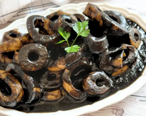 Calamares en su tinta, un plato tradicional español, servido en una fuente blanca con perejil fresco.