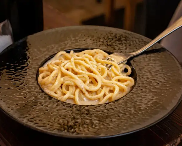 Pyszne cacio e pepe na czarnym talerzu, z widocznym młynkiem do pieprzu i solniczką w tle.
