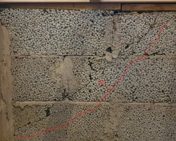 Synliga sprickor i grundmur av lättklinkerblock. En röd linje markerar en spricka som löper diagonalt över blocken.