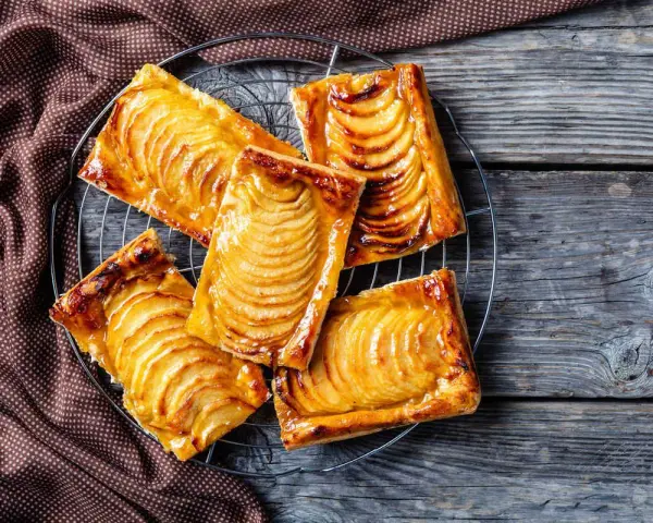 Deliziosi dolci con pasta sfoglia e mele caramellate, disposti su una gratella, su un tavolo di legno rustico.