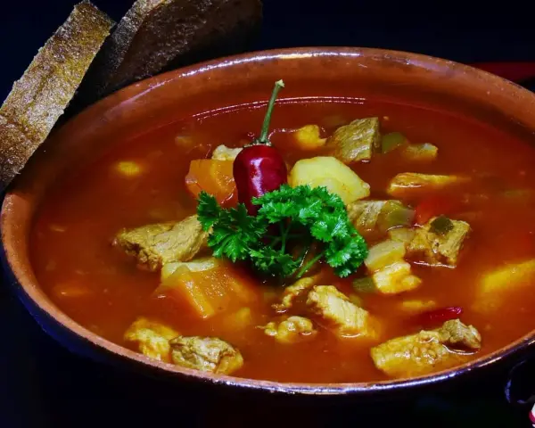 Pyszna zupa gulaszowa Ewy Wachowicz z kawałkami mięsa, ziemniaków i papryki, udekorowana papryczką chili i natką pietruszki. Podana z chlebem.