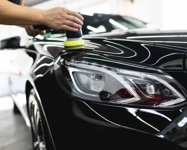A person uses a polisher to wax a shiny black car, bringing out its deep gloss.