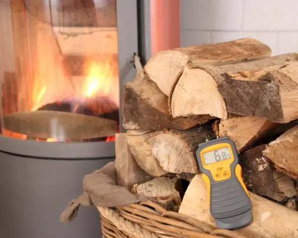 Poêle avec feu, bois de chauffage et humidimètre affichant 6.8%.