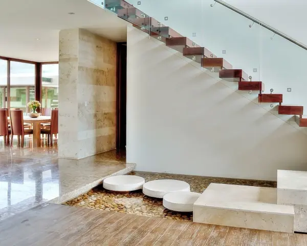 Escalera de madera flotante con barandilla de cristal. Ideas para decorar una escalera de madera con un estanque de guijarros y piedras.