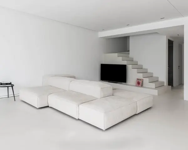 Soggiorno minimalista con divano modulare bianco e pavimento in resina lucida. Scale moderne integrano la TV.