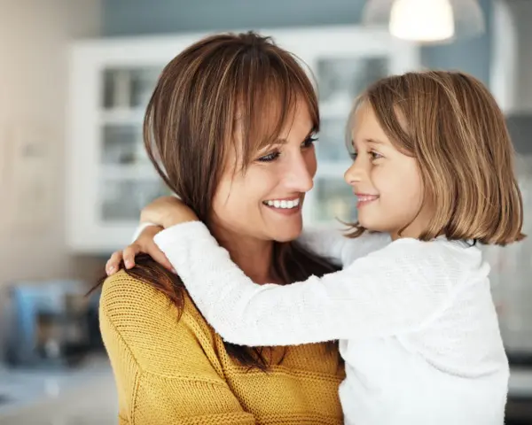 Uśmiechnięta mama i córka przytulają się, emanując ciepłem i bliskością. To kwintesencja rodzicielstwa bliskości.