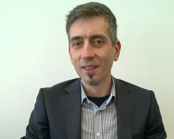 Maciej Kasprzak w czarnym garniturze i koszuli w kratę, z charakterystyczną bródką.