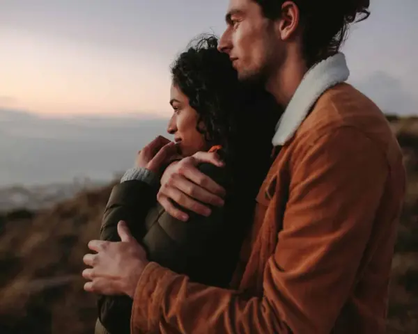 A couple embraces, looking out at a hazy landscape. This image shows how to feel more connected through shared moments and physical closeness.