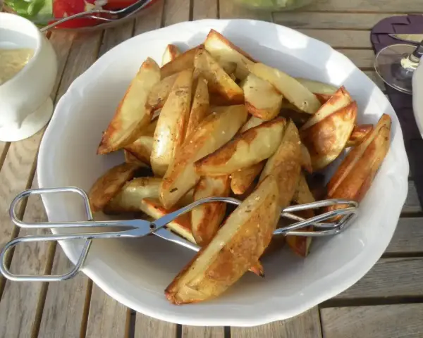En skål med gyllene klyftpotatis i ugn, redo att serveras med tång.