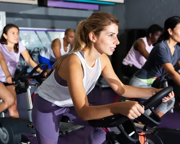 Women in a gym class experience the hiit cycling benefits, pedaling intensely on stationary bikes.