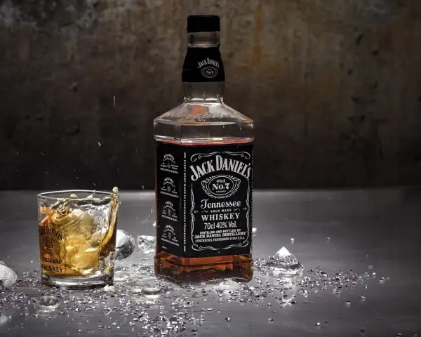 Butelka Jack Daniel's i szklanka z whisky, w której widać plusk. To klasyczny, old fashioned przepis na drinka.