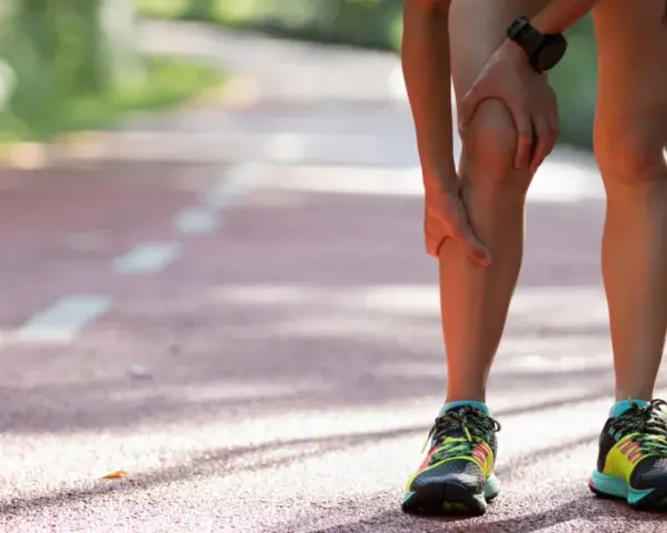 Läuferin hält schmerzendes Knie auf Laufbahn. Knieschmerzen nach Joggen sind ein häufiges Problem.