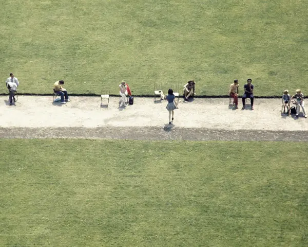 Luigi Ghirri uchwycił ludzi siedzących na krzesłach na tle zielonej trawy.