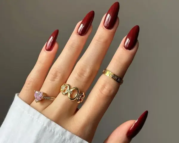 Main d'une femme aux ongles longs et pointus, vernis d'un profond couleur vernis automne. Bagues dorées ornées de pierres et de motifs.