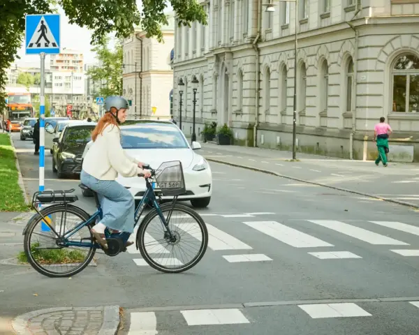 Kvinna på elcykel korsar övergångsställe. Trafik och byggnader i bakgrunden. Elcykel regler är viktiga för säkerheten.