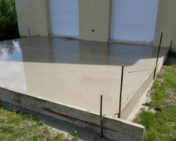 Dalle en béton fraîchement coulée pour une maison, avec coffrage en bois et ferraillage apparent. L'épaisseur de la dalle est visible.