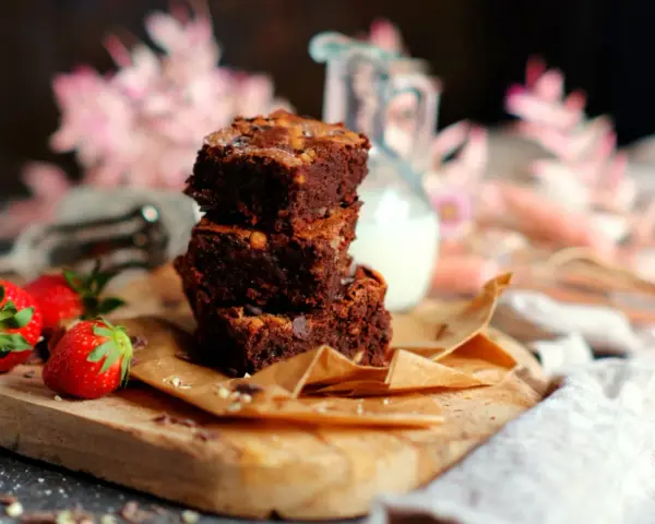 Saftige brownies rezept: Ein Stapel Schokoladenkuchen mit Nüssen, garniert mit frischen Erdbeeren und einem Krug Milch.