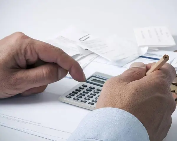 Manos calculando con calculadora y lápiz, rodeado de recibos y monedas. ¿Qué significa grupo de cotización 10?