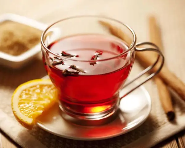 Té rojo con clavo y naranja, ideal para disfrutar de sus propiedades. Azúcar y canela al lado.