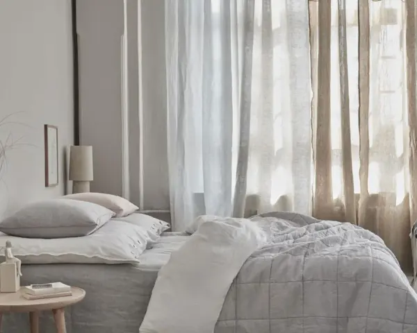Sanfte Gardinen Ideen für ein Schlafzimmer: Leinenstoffe in Weiß und Beige schaffen eine luftige Atmosphäre über einem gemütlichen Bett.
