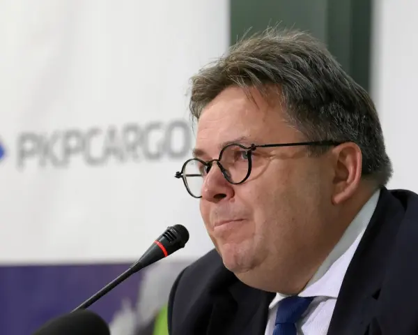 Mężczyzna w okularach przed mikrofonem na tle logo PKP Cargo.
