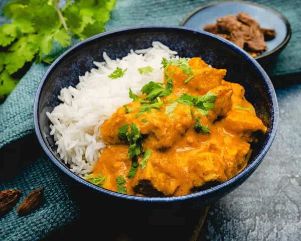 Cremiges Chicken Korma mit Basmatireis, garniert mit frischem Koriander. Ein köstliches indisches Gericht.
