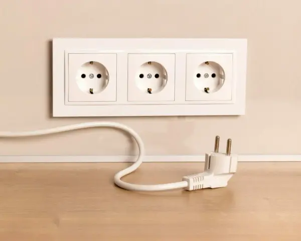 Biały kabel z wtyczką leży na drewnianym blacie obok potrójnego gniazdka. Jak schować kable, by wyglądały estetycznie?