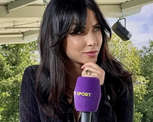 Maja Strzelczyk, dziennikarka sportowa, z mikrofonem Polsat Sport. W tle zielone drzewa i niebo.