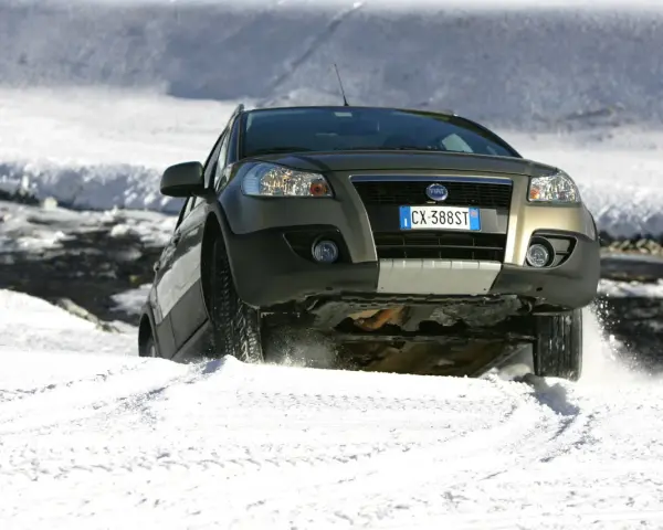 Un'auto con gomme invernali neve affronta un pendio innevato, sollevando spruzzi di bianco.