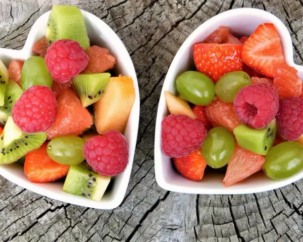 Dwa sercowate talerzyki pełne kolorowych, pokrojonych owoców: truskawek, malin, kiwi, winogron i grejpfruta. Idealne zdrowe przekąski dla dzieci.