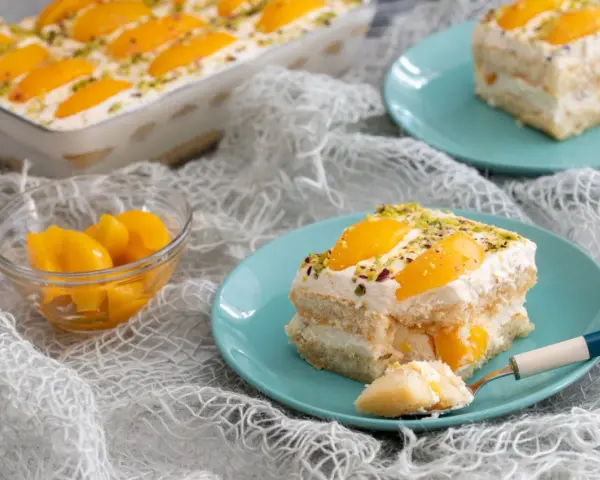 Delizioso tiramisù alle pesche, con strati di savoiardi, crema soffice e pesche sciroppate, guarnito con pistacchi.