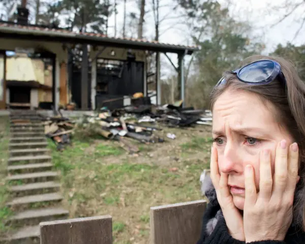 Verzweifelte Frau vor ihrem abgebrannten Haus. Die Versicherung zahlt nicht, ihr Leben liegt in Trümmern.