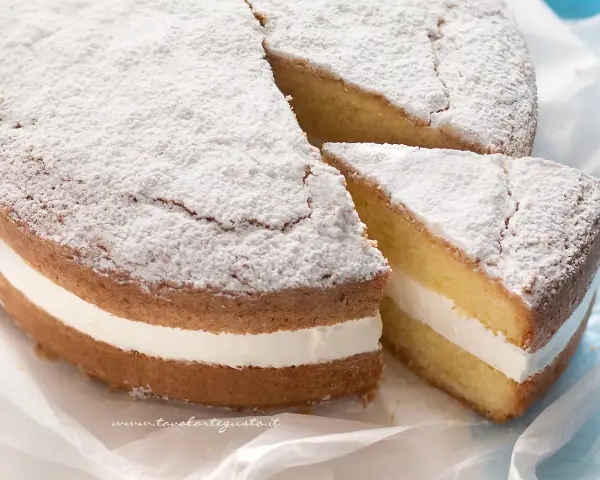 Torta paradiso sofficissima, con crema bianca e zucchero a velo. Una fetta è stata tagliata, invitando a gustarla.